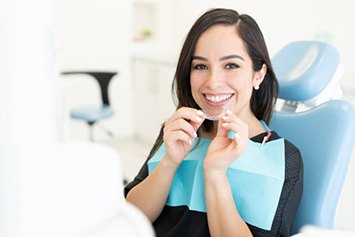 Smiling woman in dentists chair holding clear aligner