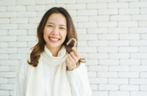 Woman in white sweater holding Invisalign in Waco.
