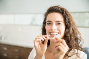 Woman smiling and holding aligner for Invisalign in Waco.