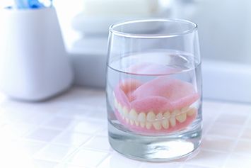 Full dentures in Waco soaking in solution on bathroom counter