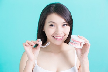 Woman holding Invisalign tray and model smile with braces