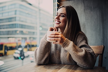A cheerful girl enjoying her porcelain veneers in a coffee shop