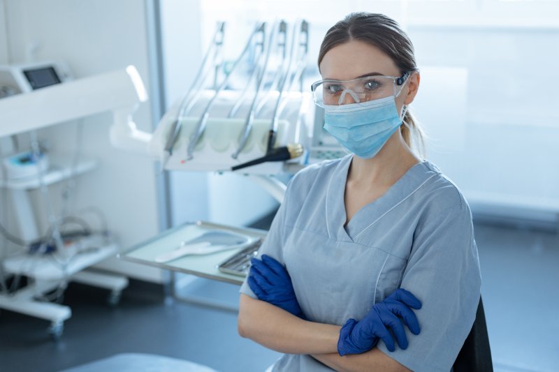 a dental team member wearing gloves, protective eyewear, and a face mask in preparation for a new patient