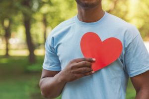 man holding a red paper heart to his chest for American Heart Month 