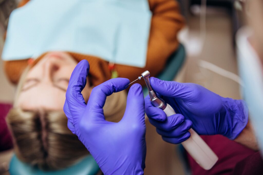 Dentist in blue gloves preparing to perform root canal on woman in dental chair